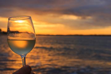Female hand with a glass of white wine on the background of a beautiful sunset.  Travel vacations concept.