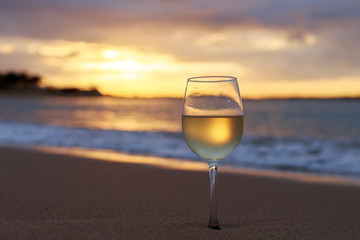 A glass  of white wine on the beach at sunset. Travel vacations concept.