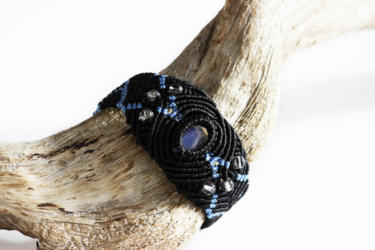 wooden curve stick and a black bracelet on the hand of waxed thread, plastic beads and moonstone in the technique of macrame.
