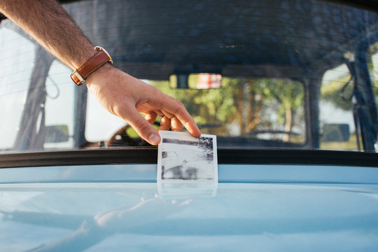 Male Hand Holding Black and White Instant Photograph of Vintage Car on Vintage Car Hood