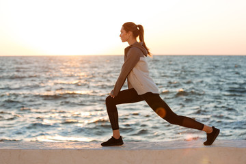 Fototapeta na wymiar Photo of fit young woman doing stretching exercise at the seaside