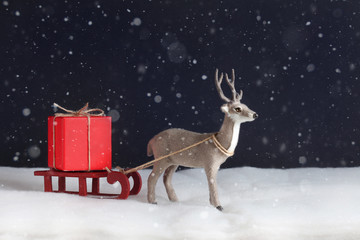 The toy deer delays sledge with a red gift box. New Year's and Christmas card