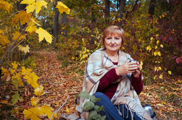 Middle-aged woman drinks tea in autumn forest