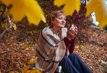 Middle-aged woman drinks tea in autumn forest