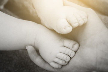 Baby feet in mother hand. Tiny newborn baby feet, concept of happy family and family support, black and white photo. Instagram yellow filter