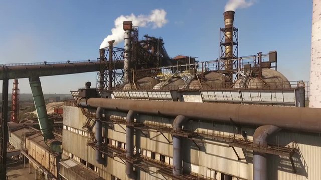 aerial video camera of the plant, the camera is moving forward, the blast furnace is working, a lot of smoke is coming from the pipes