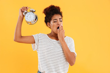 Tired african woman yawns and holding alarm clock