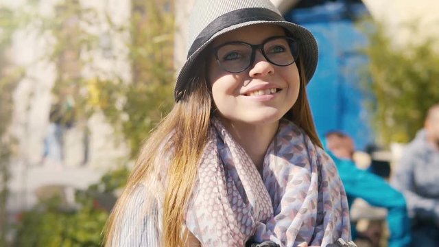 Smiling tourist girl, in striped hat and coloured scarf, walking down the street with camera, slowmotion on sunny autumn day
