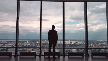 Rear view of man in formal suites who stand in front of panoramic window with city view. a man stands in front of big panoramic wiindow view from back. © Media Whale Stock