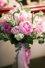 Rustic wedding bouquet with white roses, crimson peonies, and greens on a wooden floor. Indoors.