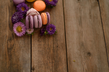 Obraz na płótnie Canvas Violet and yellow macarons and flowers on wooden table background. Colorful french dessert with fresh flowers. Autumn concept