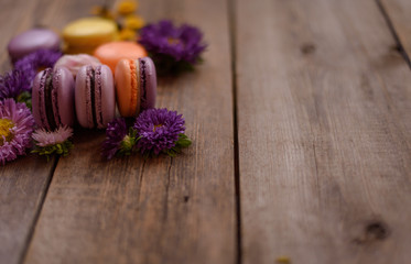 Violet and yellow macarons and flowers on wooden table background. Colorful french dessert with fresh flowers. Autumn concept