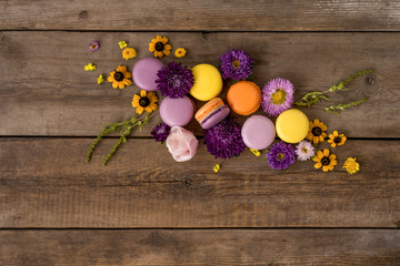 Macarons and flowers wreath on wooden table background. Colorful french dessert with fresh flowers. Top view