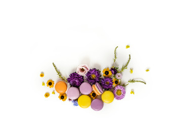 Macarons and flowers wreath on a white background. Colorful french dessert with fresh flowers. Top view