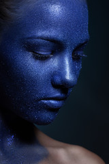 portrait of young beautiful girl. face painted with blue paint and glitter.
