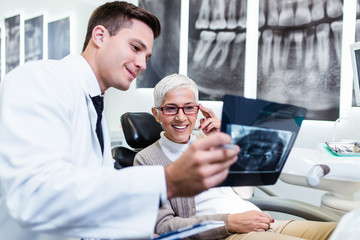 Handsome and attractive male dentist looking at dental x-ray together with his beautiful senior...