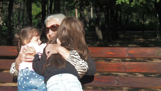A happy grandmother hugs her granddaughters. Elderly woman with children in the park.