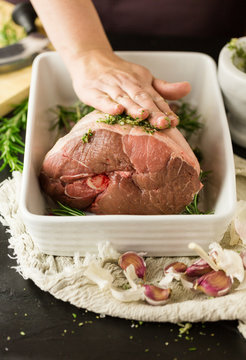Woman rubbing herb, garlic and oil paste onto leg of lamb
