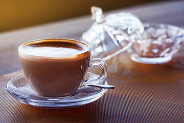  a glass cup with cappuccino stands on a table, next to a crystal sugar bowl. Horizontal orientation