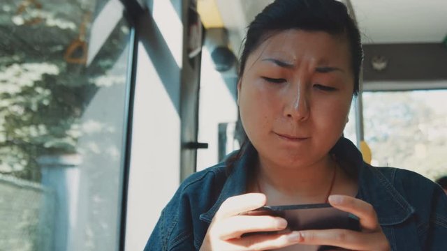 Closeup portrait of smiling mature fatty asian women riding in public transport and changing emotions on her face from happy to depressive using smartphone phablet mobile digital technologies. Shot on