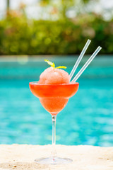 Frozen strawberry margarita cocktail at the edge of a resort pool.  Concept of luxury vacation