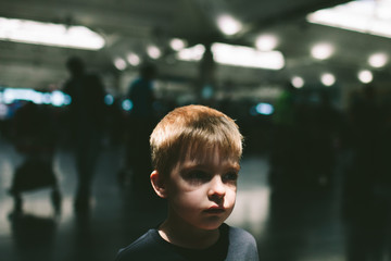 Close up of a young boy standing alone in a busy place with shadowy figures and blurred lights.
