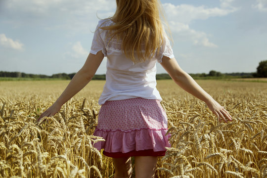 woman in pink skirt from the back in a wheat field