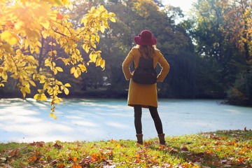 Beautiful woman tourist with backpack in park. Young girl standing over lake in autumn season.