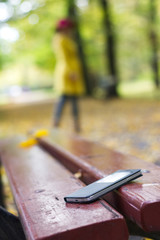 Forgotten smartphone on a park bench. Woman is leaving from a bench where she lost her cell phone. 