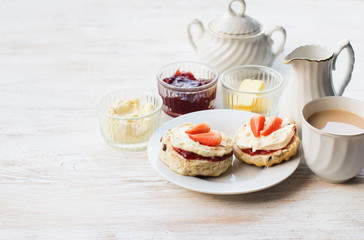 English scones with butter, jam and cream, tea with milk on the white wooden table, selective focus copy space for text
