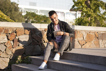 Happy young man reading on a tablet or listening to music on the stairs