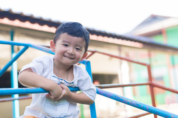 Asian boy hang the metal bar at outdoor playground.