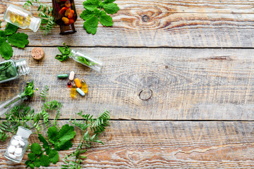 Healing herbs. Fresh leaves, bottles and pills on wooden background top view copyspace