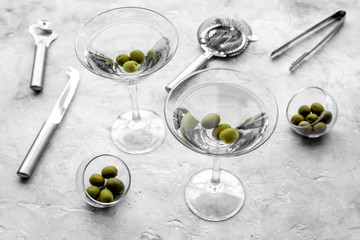 Make martini cocktails. Glass with beverage, olives and utensils on grey stone background top view