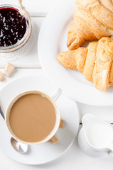 Traditional breakfast with fresh croissants and coffee on white wooden background.