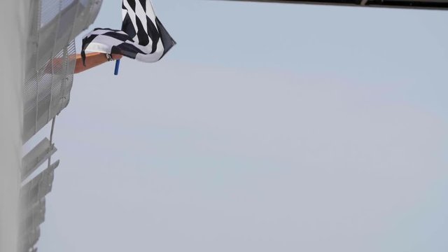Man holding and waving Checkered race flag in slow motion at finish line on a raceway. Victory, achievement, success and sport concept.