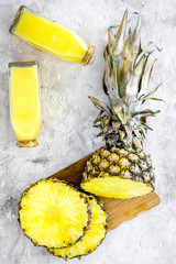 Non-alcoholic beverages. Bottle with fruit juice near pineapples slices on grey background top view