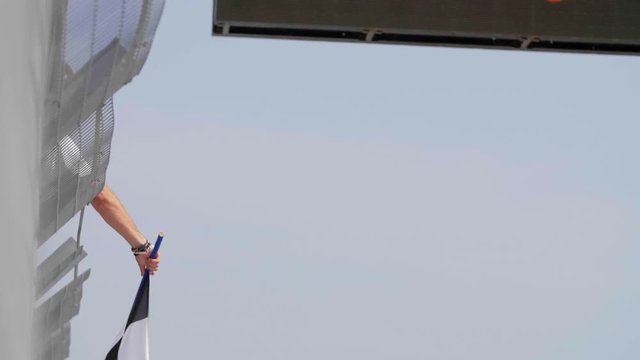 Man holding and waving Checkered race flag in slow motion at finish line on a raceway. Victory, achievement, success and sport concept.