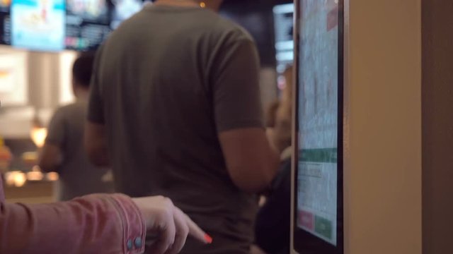 Woman choosing food via self-service machine at fast food restaurant. Girl using self-service touch terminal