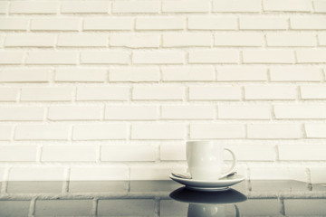 white cup of hot coffee on top of glass table with white brick wall background. concept fot drink and food