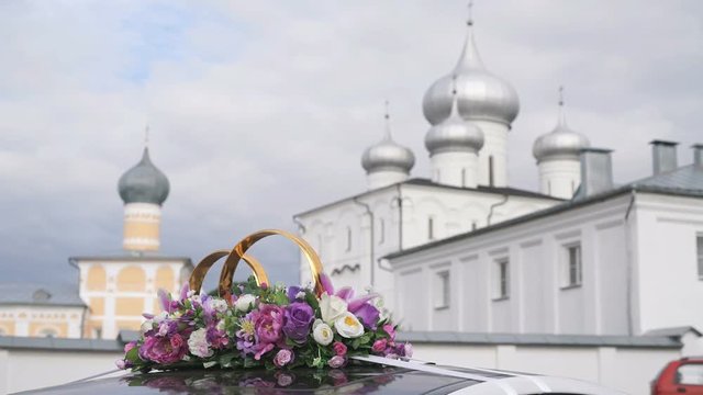 Wedding decorations and scenery in view golden rings by car roof in the background of the Orthodox monastery with the crosses on the domes