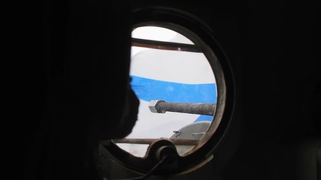 From the round window of an armored troop-carrier is seen a developing blue-white flag and cannon barrel