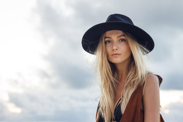 Close up of beautiful young blonde woman with black hat. Wearing brown vest. Her long messy hair looks amazing.
Professional makeup, hairstyle and styling.