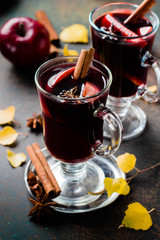 Mulled wine hot drink with citrus, apple and spices in glass on dark concrete background. Autumn hot drink. Fall autumn leaves