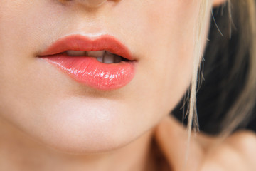 Fototapeta premium Detail on a gorgeous lips of a beautiful happy blonde woman. Lips are painted with bright red lipstick, skin is soft and natural. Photographed on daylight, isolated on black background.