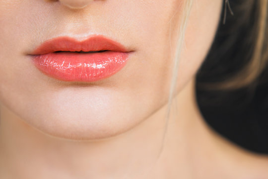 Detail on a gorgeous lips of a beautiful happy blonde woman. Lips are painted with bright red lipstick, skin is soft and natural. Photographed on daylight, isolated on black background.