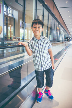 Happy asian child standing and smiling near electric speedwalk in modern airport.