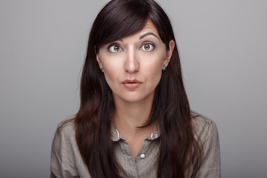 Closeup portrait of beautiful young middle age brunette Caucasian woman with brown eyes with funny emotional face expression. Girl female with long dark hair looking surprised hilarious