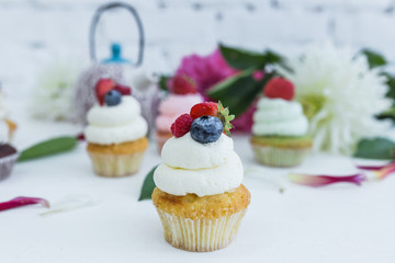 Cupcakes with fresh berries flowers and leaves, a cup of tea or coffee and a kettle.