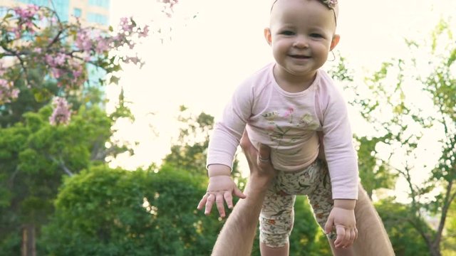 Caucasian young daddy playing with little cheerful sweety kid slow mo closeup. Father's funny joy games loves babygirl trow up in the air toss not much high, raised looking at sky, sun at spring time